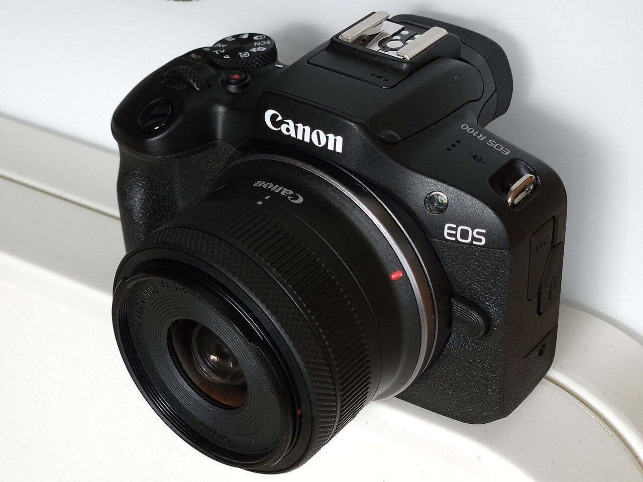 ブラックのCanon EOS R100にRF-S18-45mmレンズを装着し、斜め上から撮影した外観参考写真。